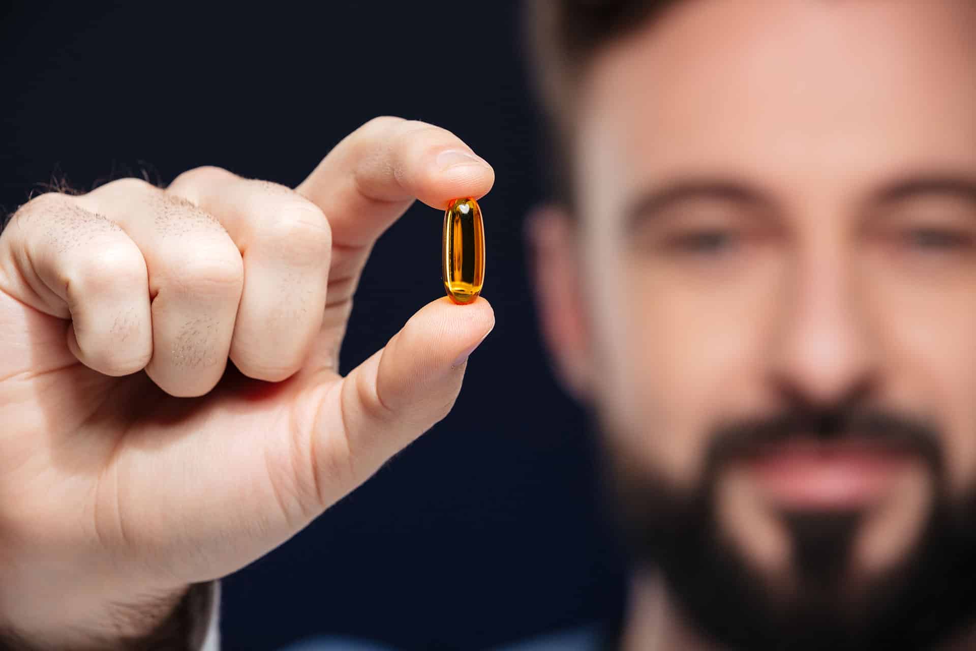 Un homme barbu tenant une capsule de vitamines.